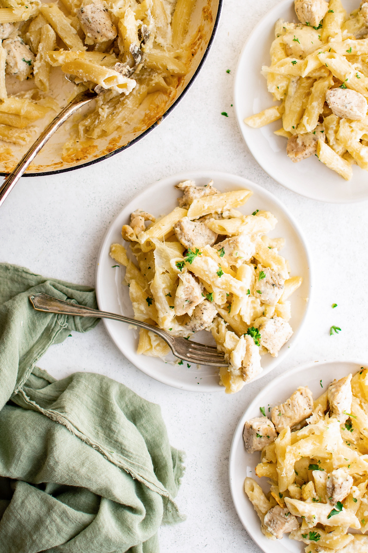 Overhead of baked chicken alfredo on a plate with a fork. Baking skillet is on the side. 