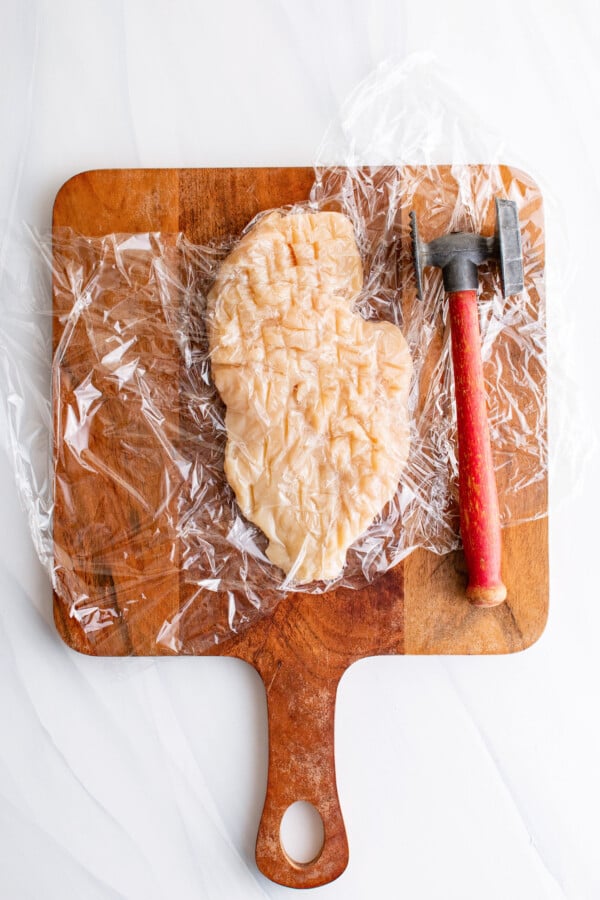 Placing the chicken in between plastic wrap. Meat mallet on the side. 