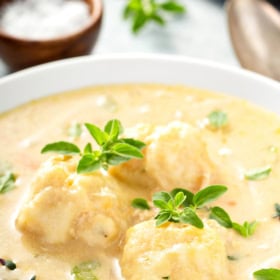 A bowl of chicken and dumplings with fresh thyme on top.