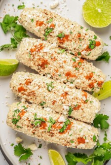 Mexican street corn on a platter with cilantro and lime wedges.