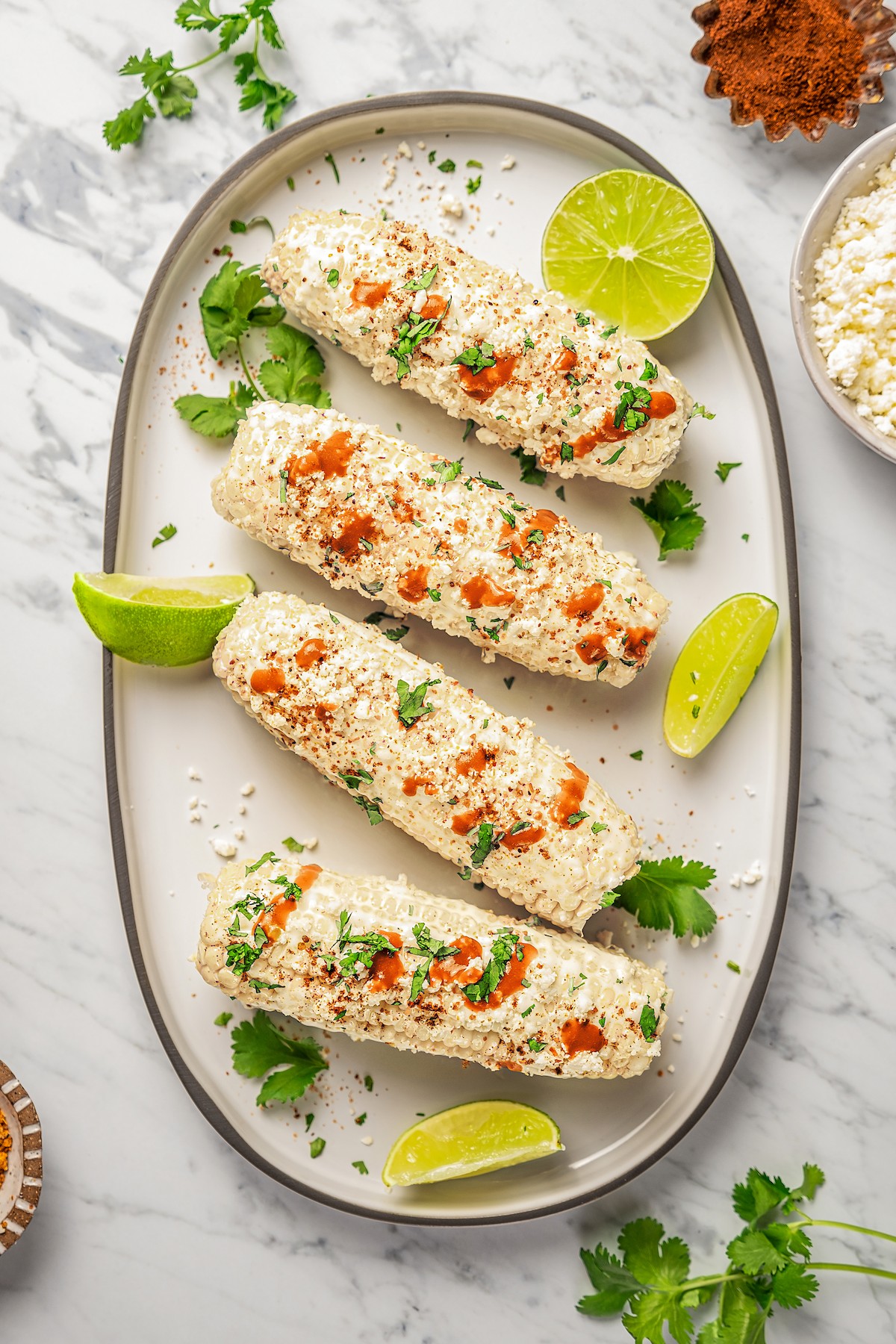 Elote on a serving platter with lime wedges and cilantro.