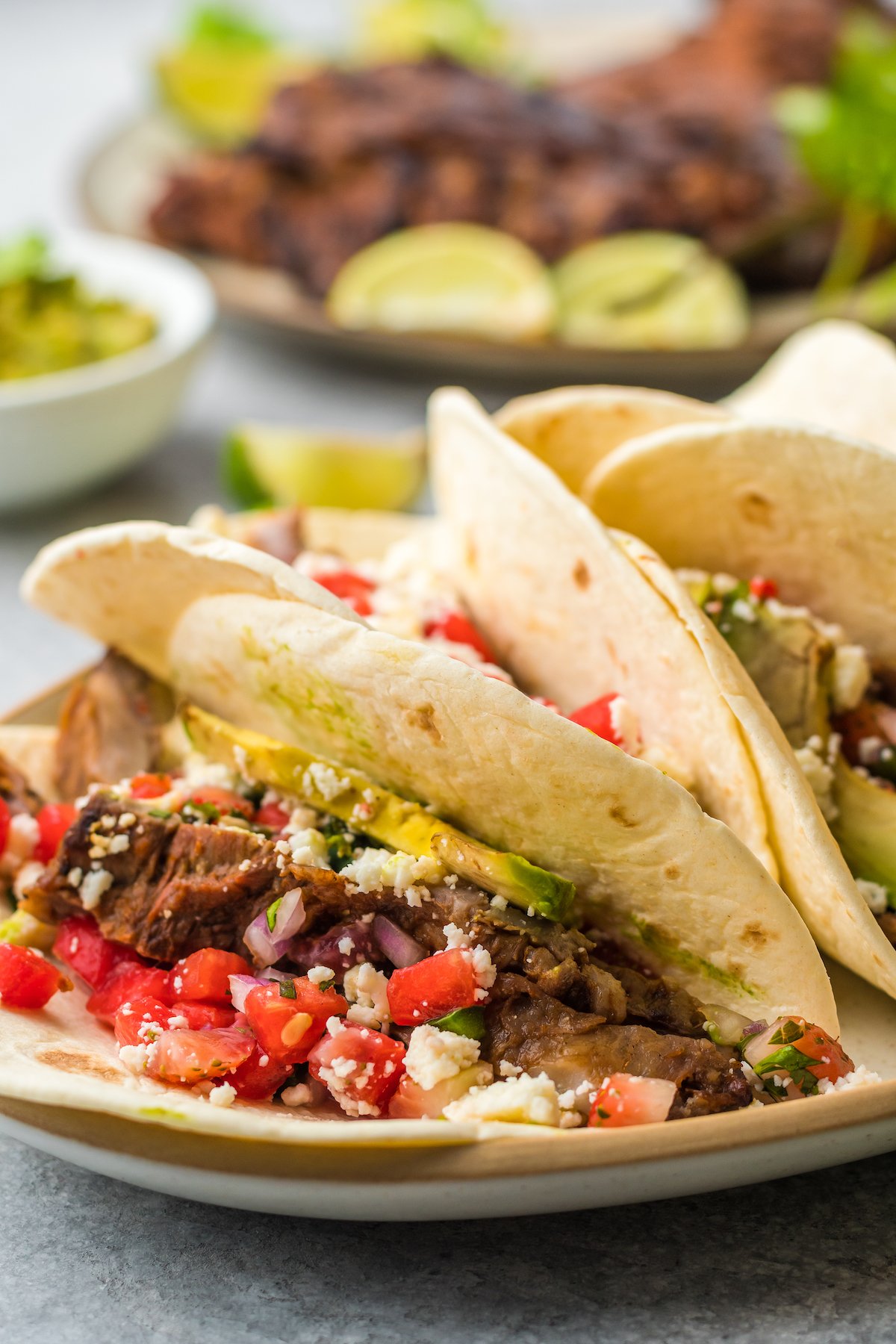 Flank steak tacos with salsa, cheese, and sliced avocado.