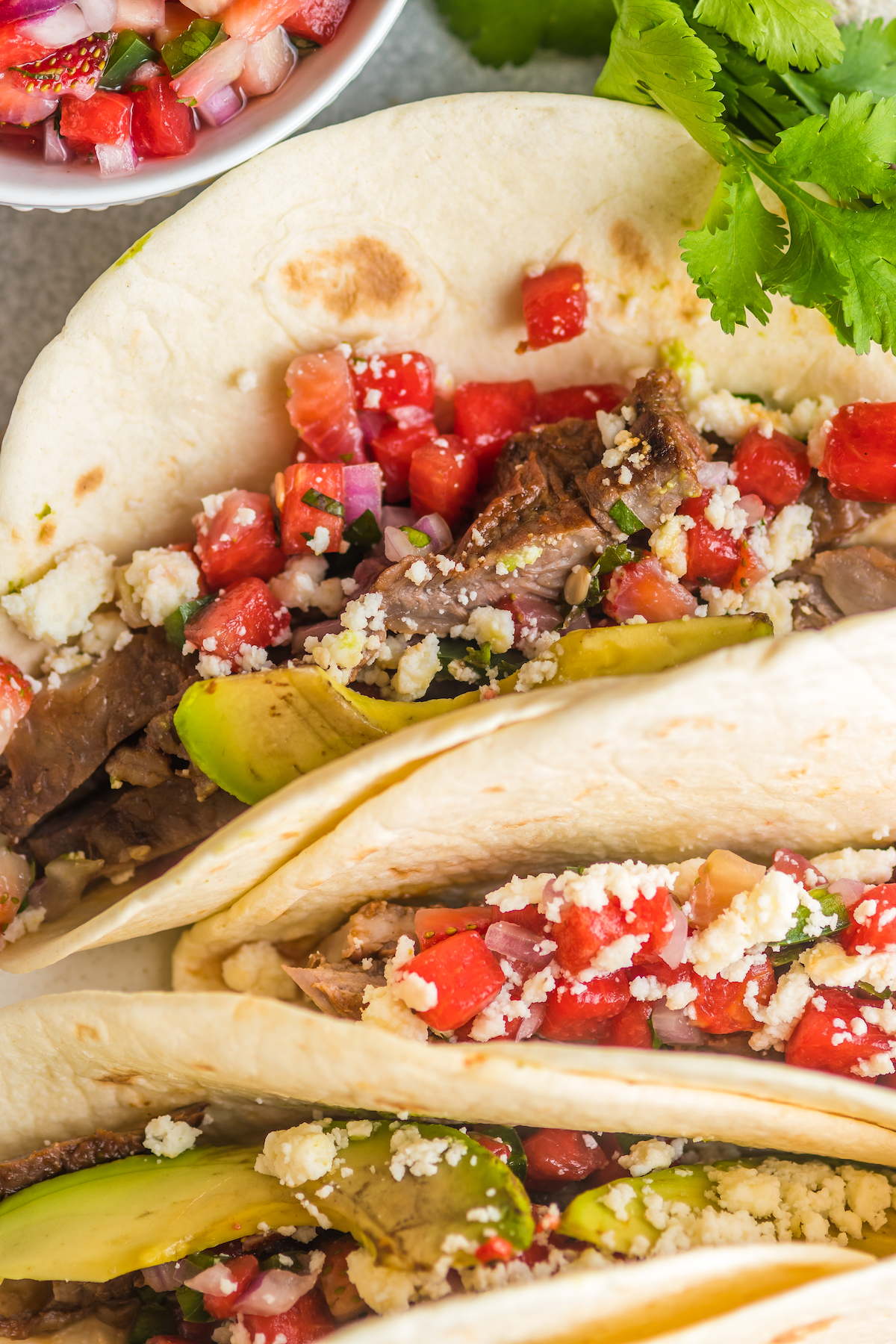 Close-up of flank steak tacos with queso fresco, salsa, and avocado. 