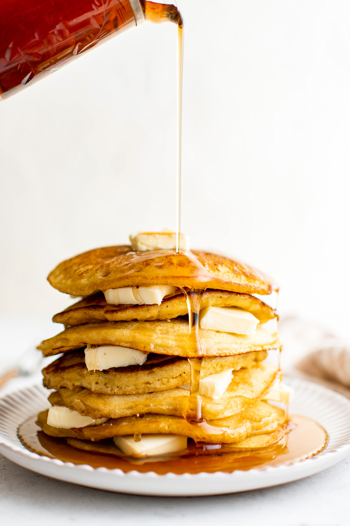 Pouring syrup over a stack of johnny cakes with pats of butter in between.