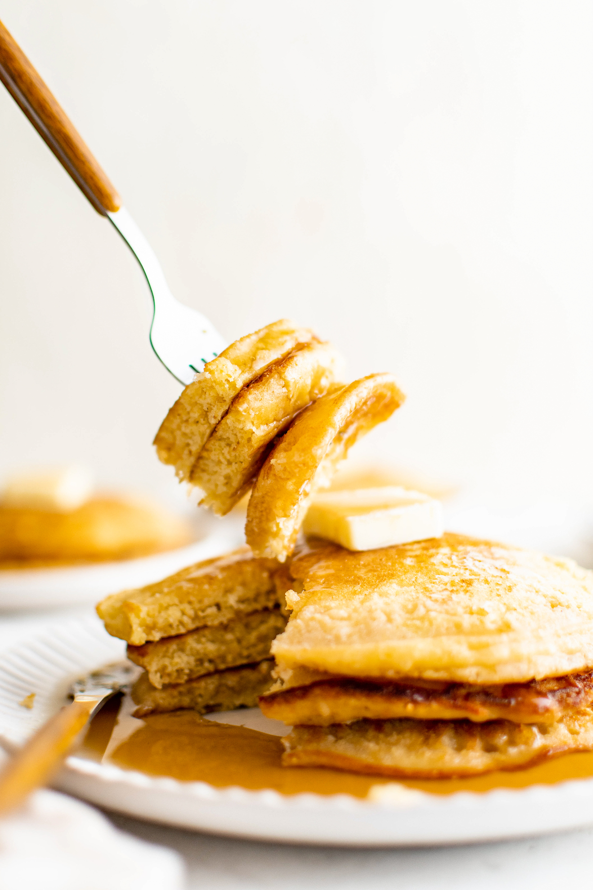 A fork lifting a bite of cornmeal pancakes from a plate.