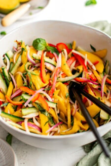 Mango salad in a white salad bowl with serving utensils.