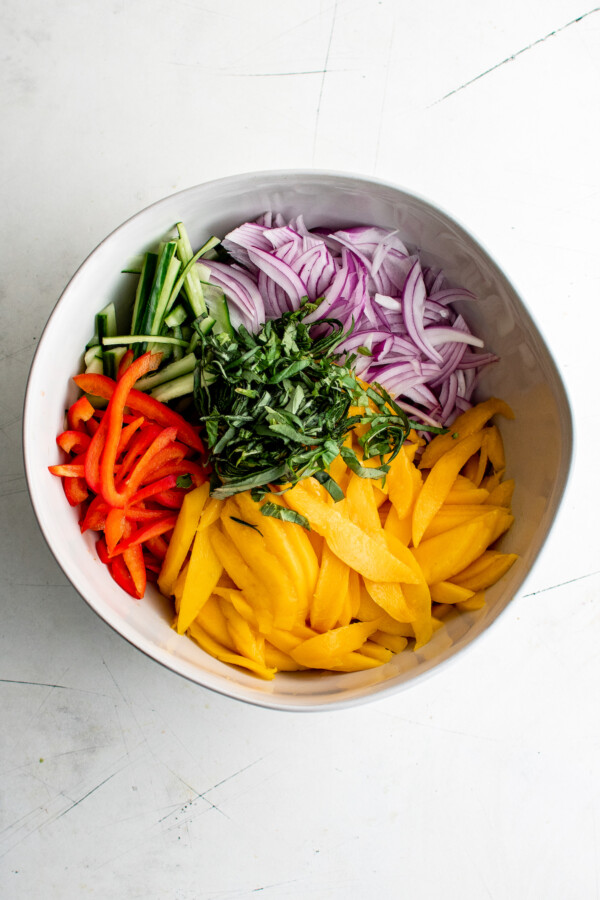Cucumber, onion, mango, bell pepper, and chopped basil in a salad bowl.