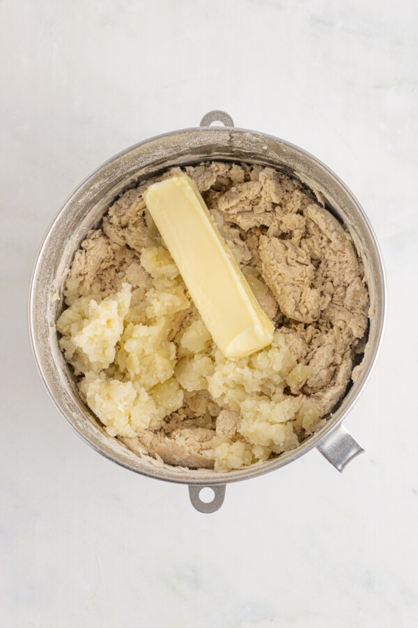 Adding butter and potatoes to bread dough in a mixer.