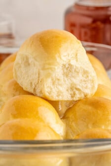 A soft dinner roll resting on top of more dinner rolls in a glass baking sheet.