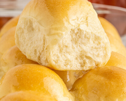 A soft dinner roll resting on top of more dinner rolls in a glass baking sheet.