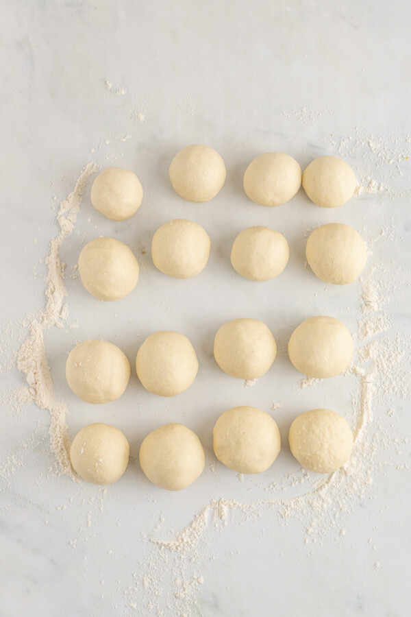 Sixteen balls of dough on a floured work surface.