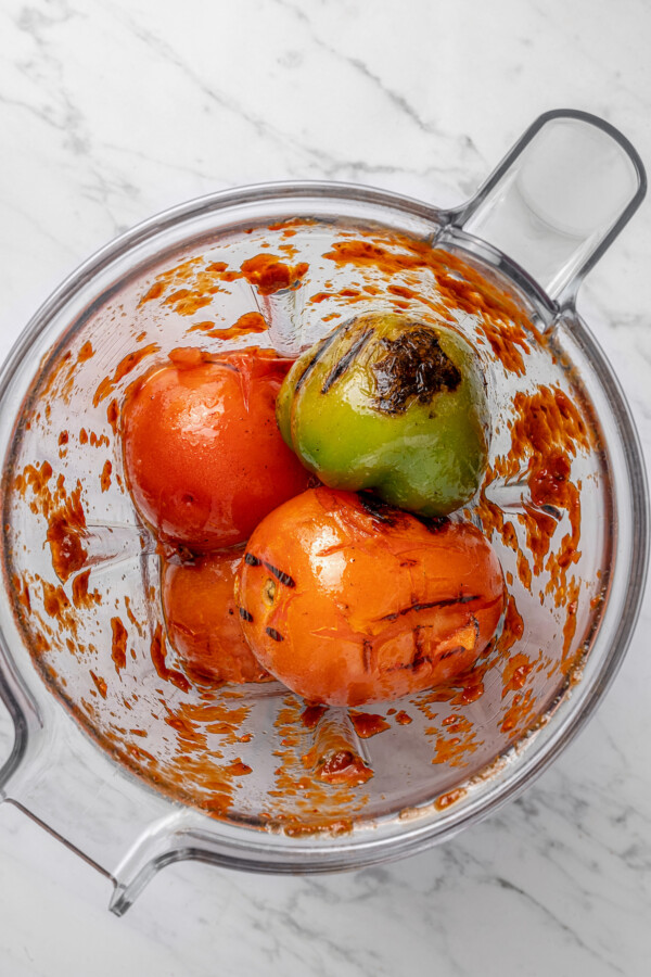 Adding the charred tomatoes and tomatillos to the blender. 