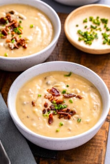 Two bowls of thick potato leek soup topped with bacon and chives.
