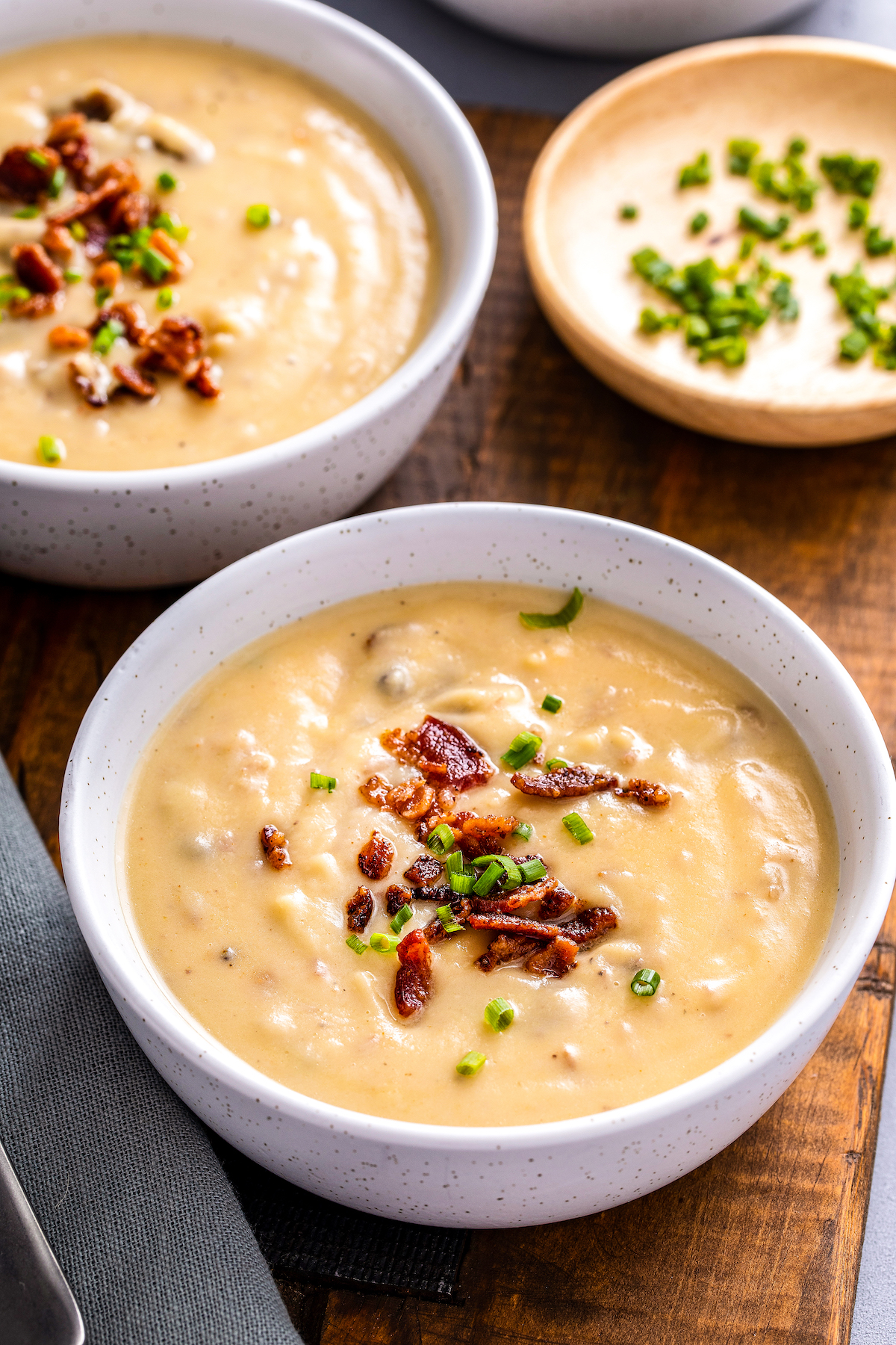 Two bowls of thick potato leek soup topped with bacon and chives.