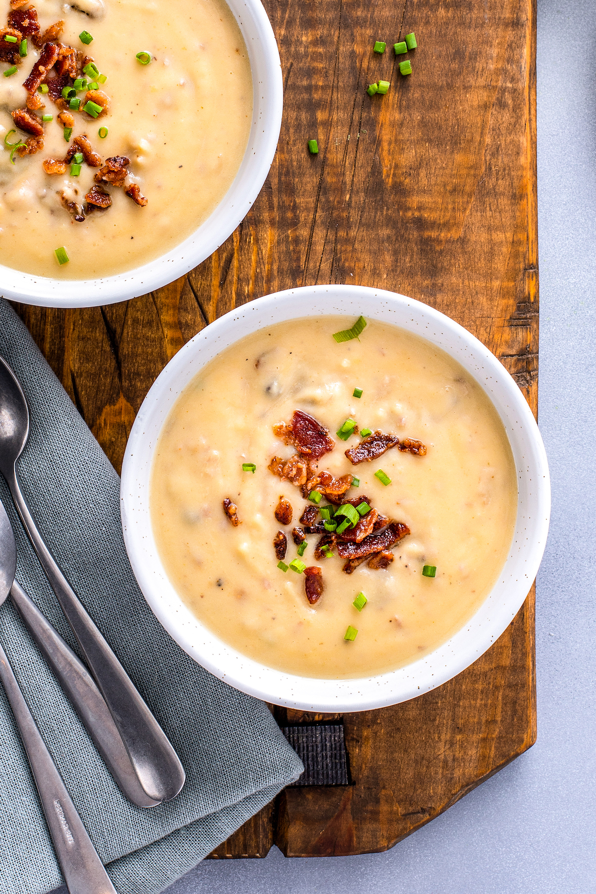 A shot of creamy potato soup with bacon and chive toppings.