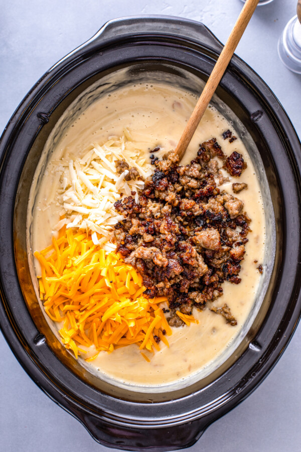 Blended potato soup in a crockpot, with sausage and cheese being stirred in.