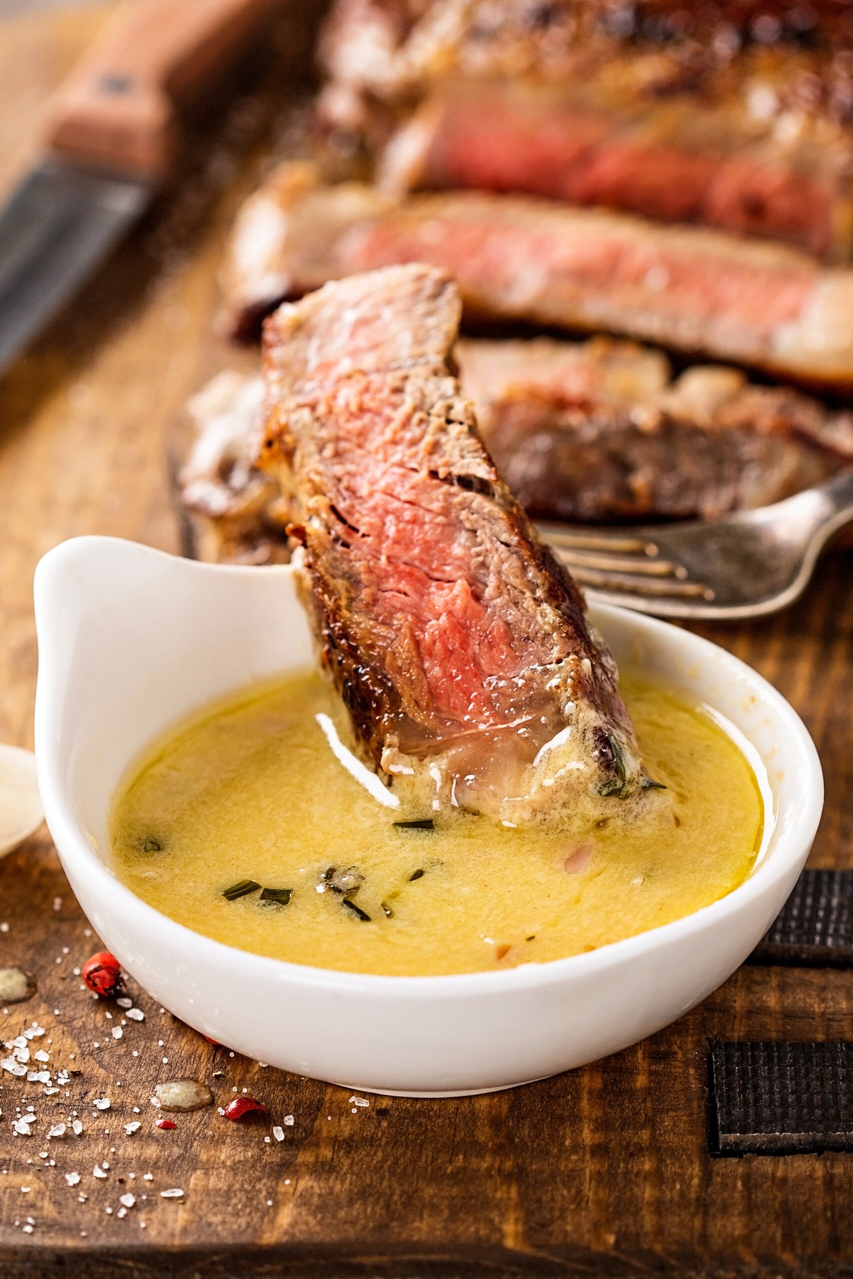 Homemade steak sauce in a bowl with a piece of steak on a fork being dunked in the buttery sauce.