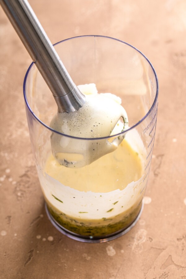 A immersion blender in a jar blending egg yolk and tarragon mixture.