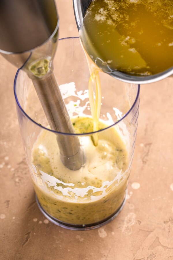 Melted butter being poured into sauce mixture in a jar being blended with an immersion blender.