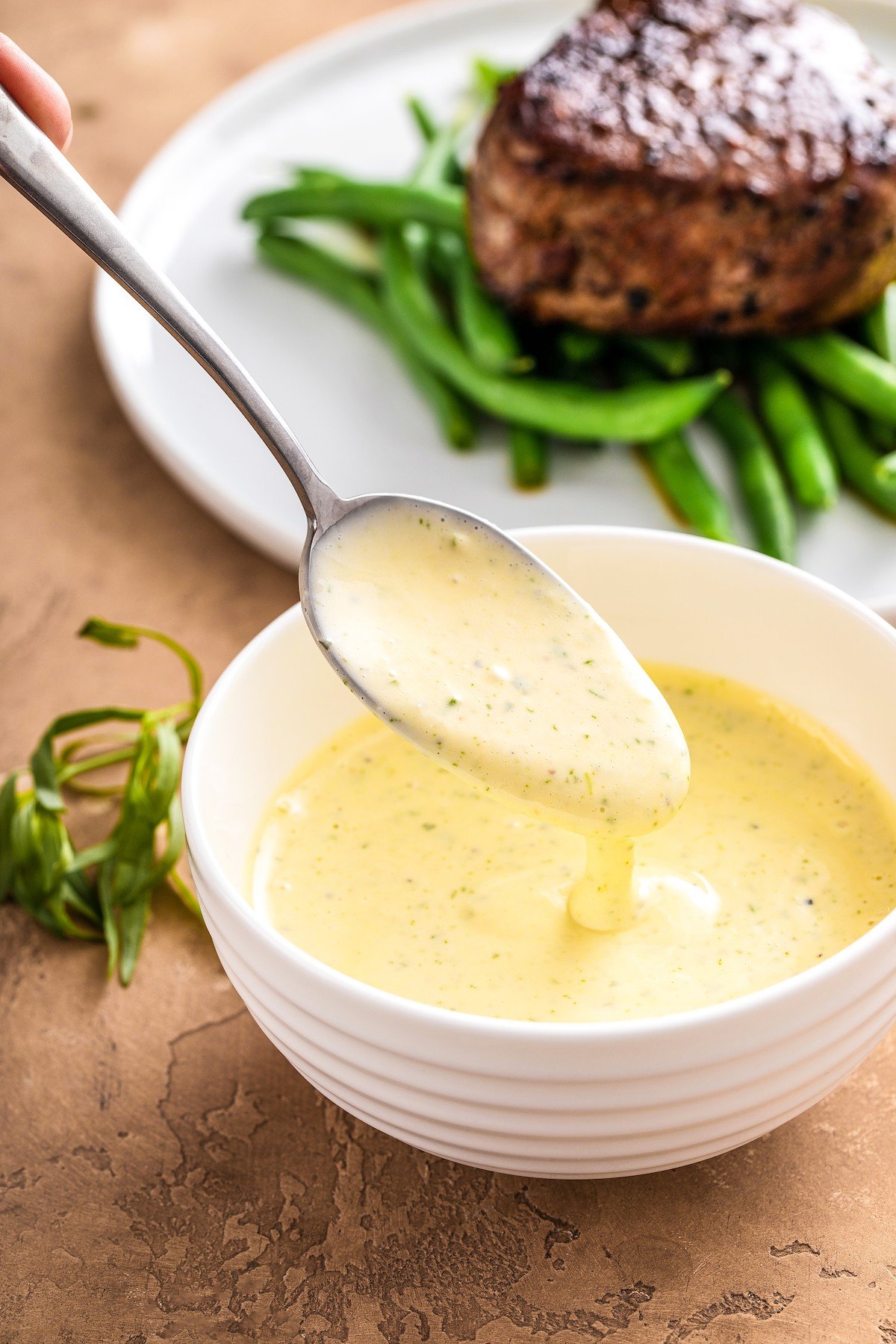 A bowl of Béarnaise Sauce with a spoon scooping up some of the sauce.