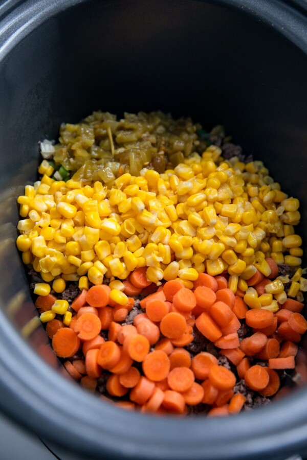 Carrots, corn, and other ingredients in a crockpot insert.