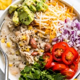 A large bowl of white chili, topped with avocado, tomato, red onion, and more.