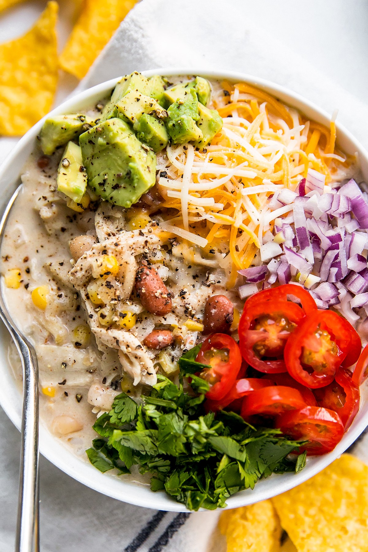 A large bowl of white chili, topped with avocado, tomato, red onion, and more.