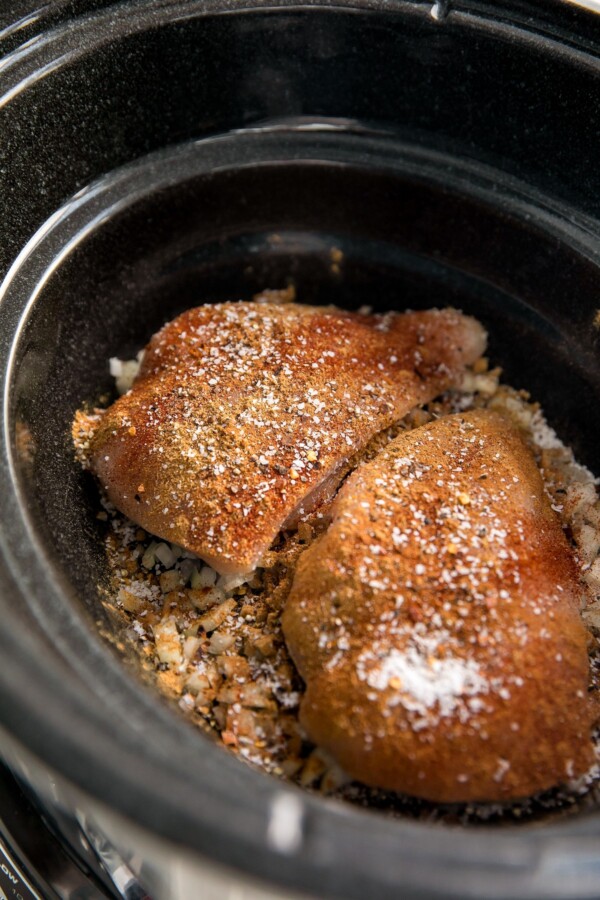 Chicken breasts, beans, seasonings, and other ingredients in a crockpot.