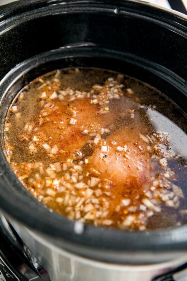 A slow cooker with chicken, broth, and other ingredients.