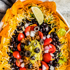 Dorito taco salad layered in a bowl with lime wedges.