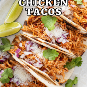 Chicken crockpot tacos on a plate with cilantro, onion and cheese on top.