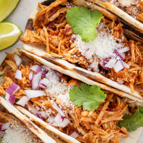 Shredded chicken tacos on a plate with red onion, cheese and cilantro.
