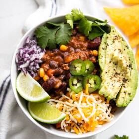 A bowl of beef chili topped with avocado, jalapeno, and more.