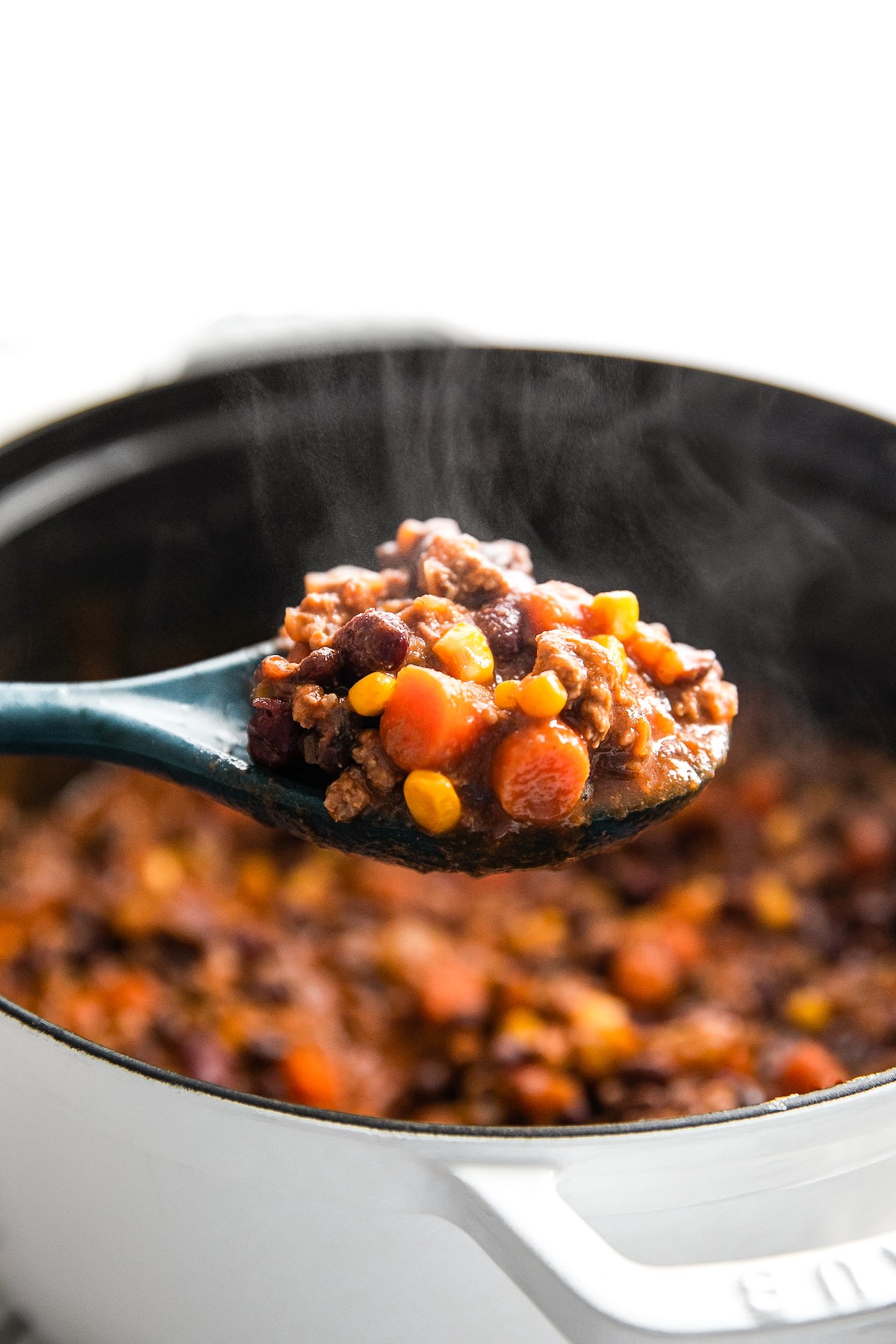 Lifting a spoonful of beef chili out of a pot.