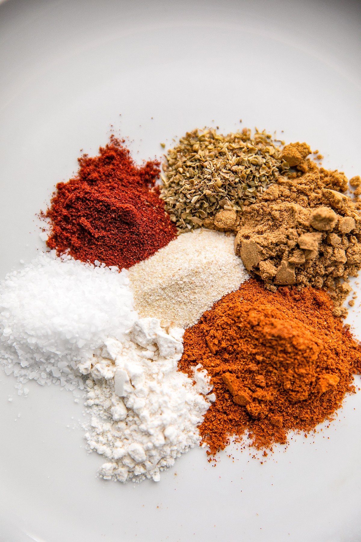 Overhead shot of spices and seasonings in little mounds on a white background.