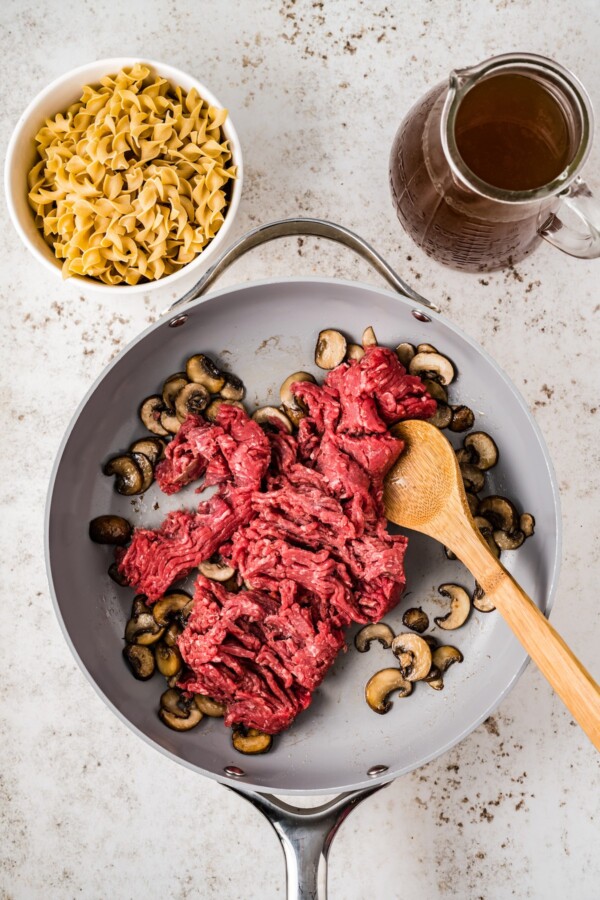 Cooking ground beef in a skillet with mushrooms.