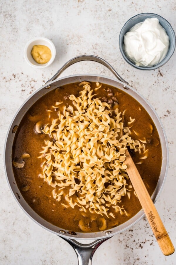 Stirring egg noodles into a skillet.