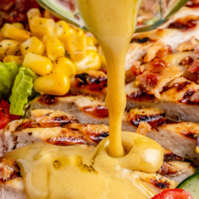 Grilled chicken salad with honey mustard salad dressing being poured on top.