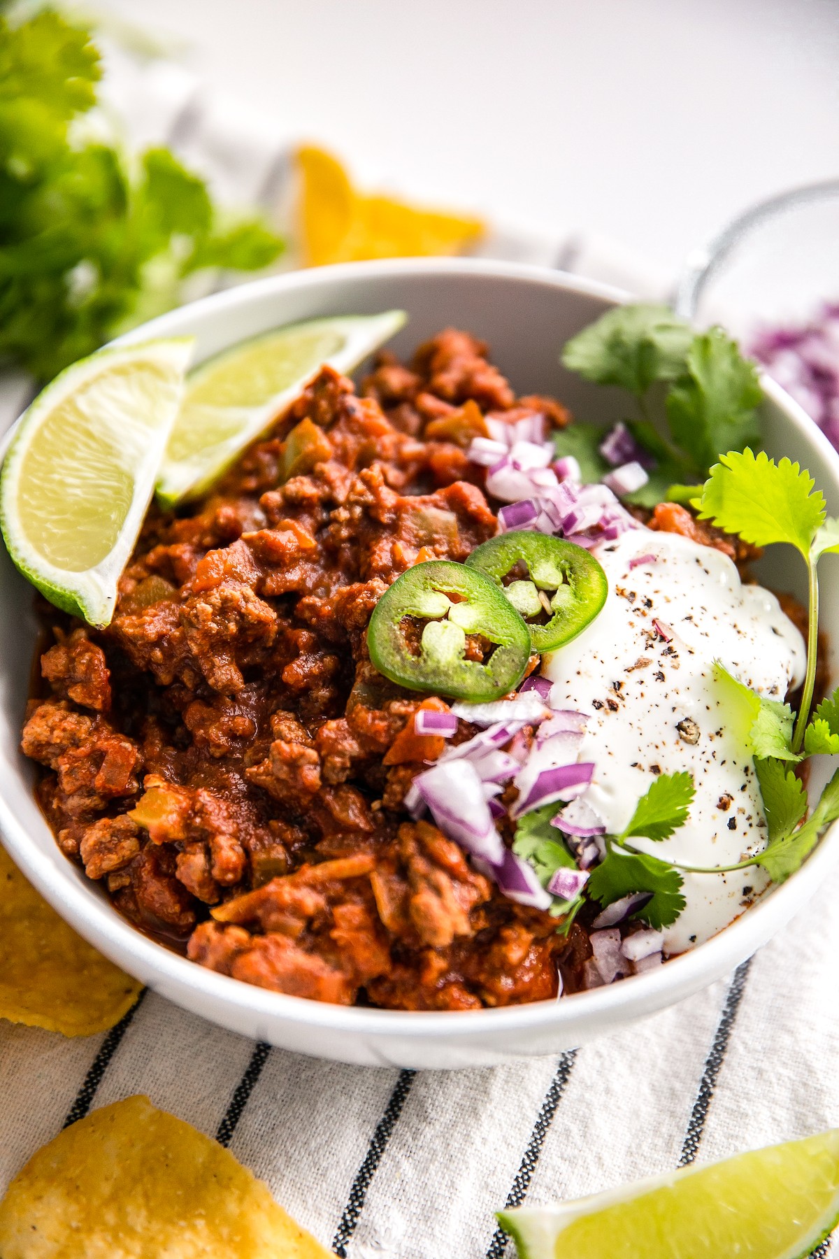 A bowl of homemade Texas chili topped with diced onion, jalapeno, cilantro, and lime.