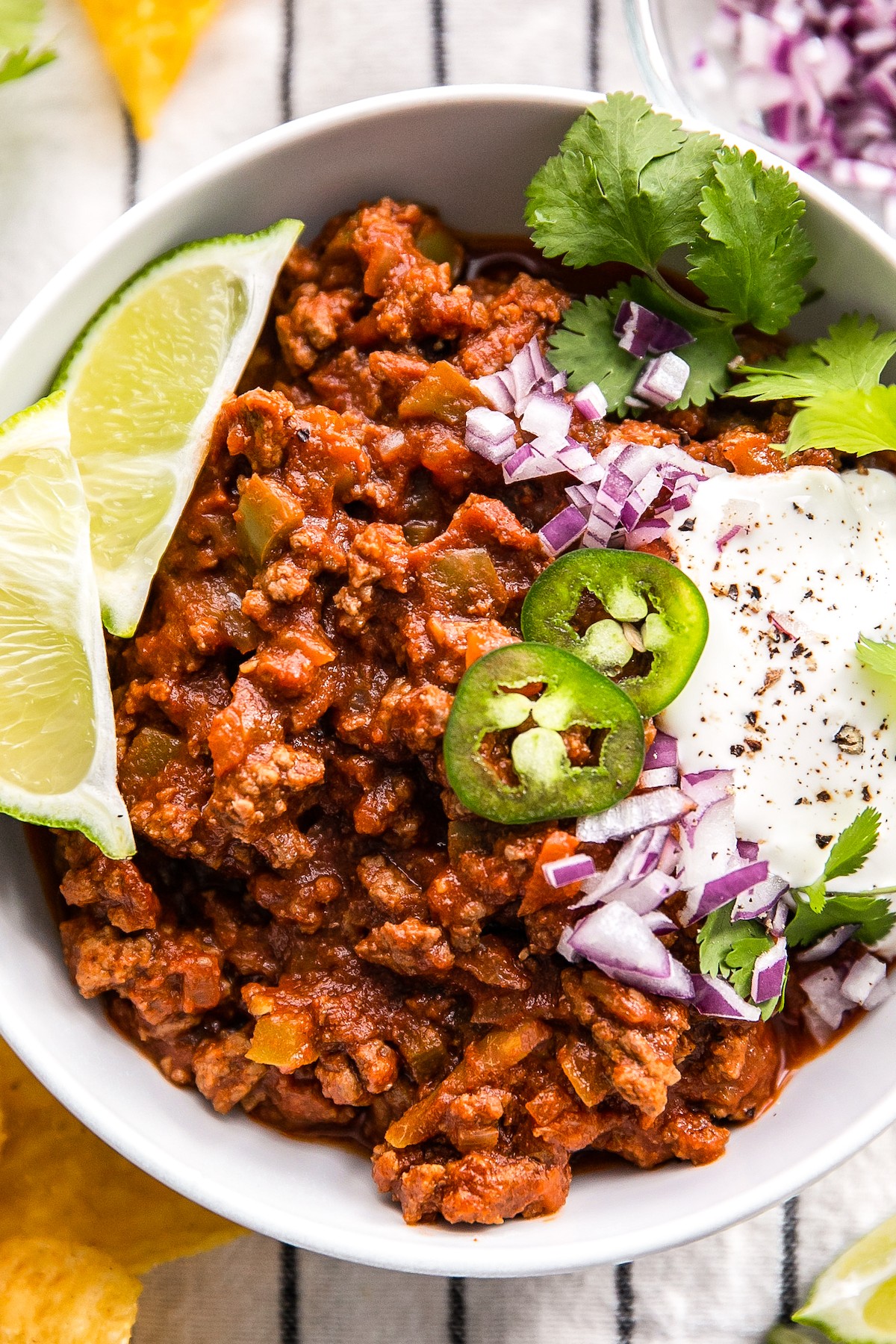 Overhead shot of a serving of chili in a white bowl, with toppings.