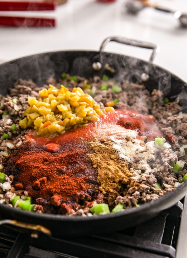 Seasonings, diced chilies, and other ingredients mixed into a skillet of cooking beef.