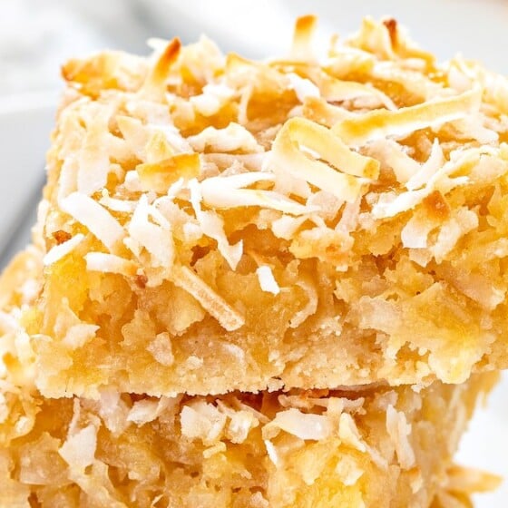 Pineapple coconut bars stacked on top of each other on a plate with a fork.