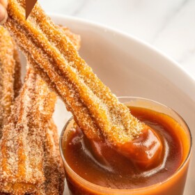 Pumpkin churro being dunked in salted caramel sauce.