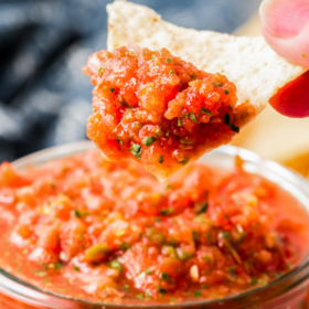 A jar of homemade salsa with a tortilla chip scooping up a bite.