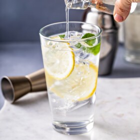 Pouring simple syrup into a glass with lemon, ice, and mint.
