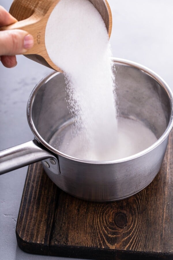 Pouring white sugar into a small saucepan.