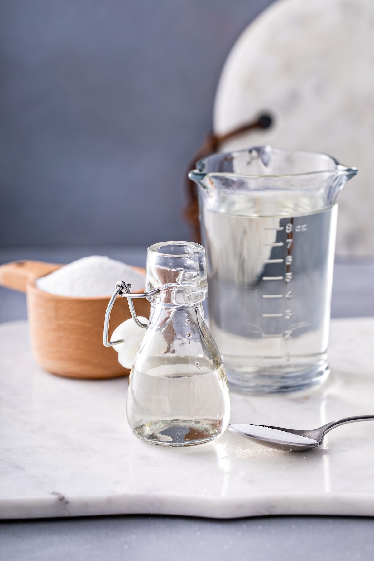A measuring cup of clear liquid, and a small glass jar with a stopper.