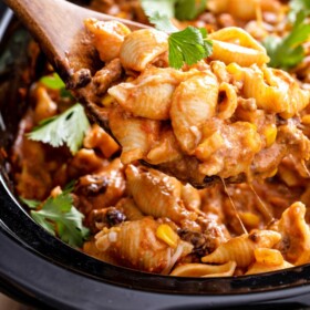 Slow cooker taco pasta with a wooden spoon scooping a serving out of a crockpot.
