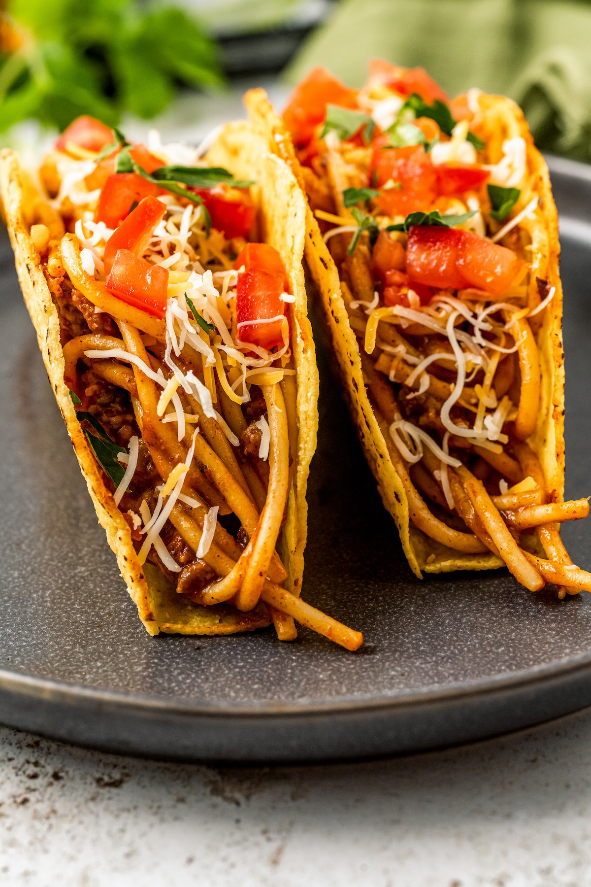 Two tacos from the side, showing the pasta inside and layers of toppings.