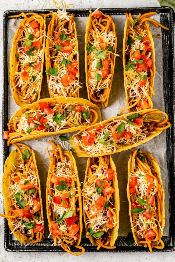 Spaghetti tacos topped with shredded cheese, tomatoes, and parsley.